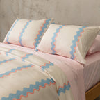 Bed with pink and blue striped bedding and pillows against a gray wall.