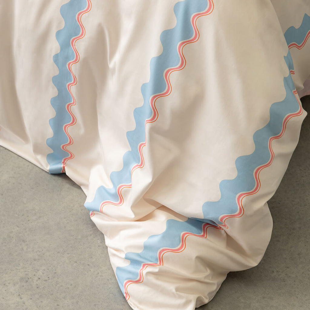 Close-up of a cream duvet cover with blue and pink zigzag trim on a neutral background.