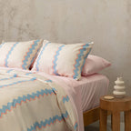 Bed with pink and blue striped bedding against a textured wall.
