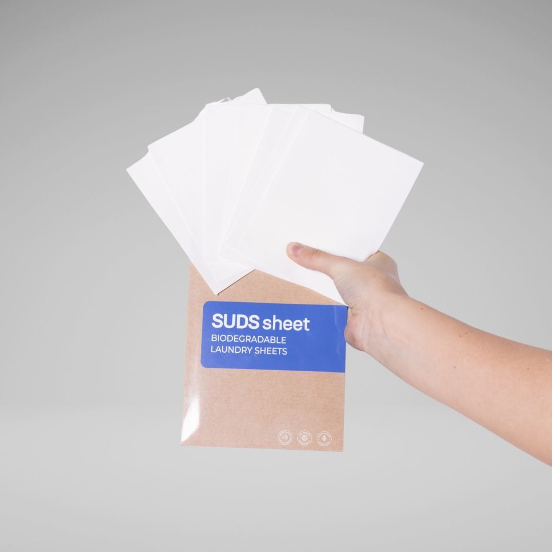 Hand holding a stack of white laundry sheets with a blue label on a gray background