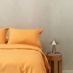 Styled bedroom scene featuring mustard yellow bedding alongside a wooden side table and metallic lamp