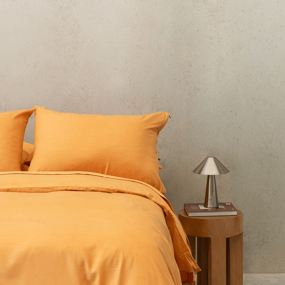 Styled bedroom scene featuring mustard yellow bedding alongside a wooden side table and metallic lamp
