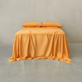 Mustard yellow bed sheet set draped over a double bed with two matching pillowcases against a textured wall