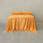 Mustard yellow bed sheet set draped over a double bed with two matching pillowcases against a textured wall