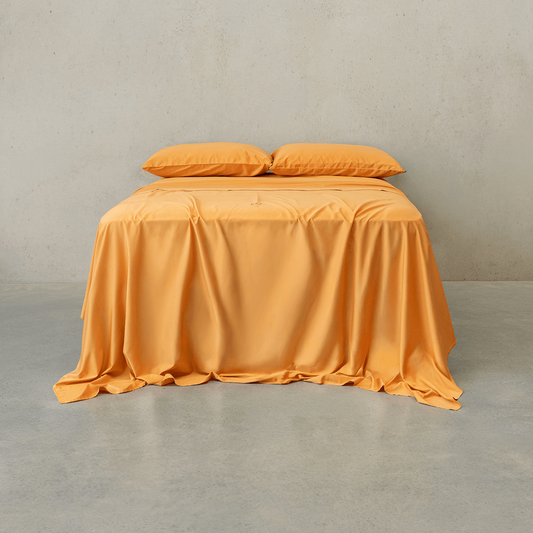 Mustard yellow bed sheet set draped over a double bed with two matching pillowcases against a textured wall
