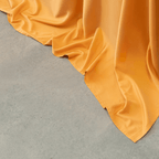 Close-up view of mustard yellow sheet fabric cascading smoothly onto a gray concrete floor