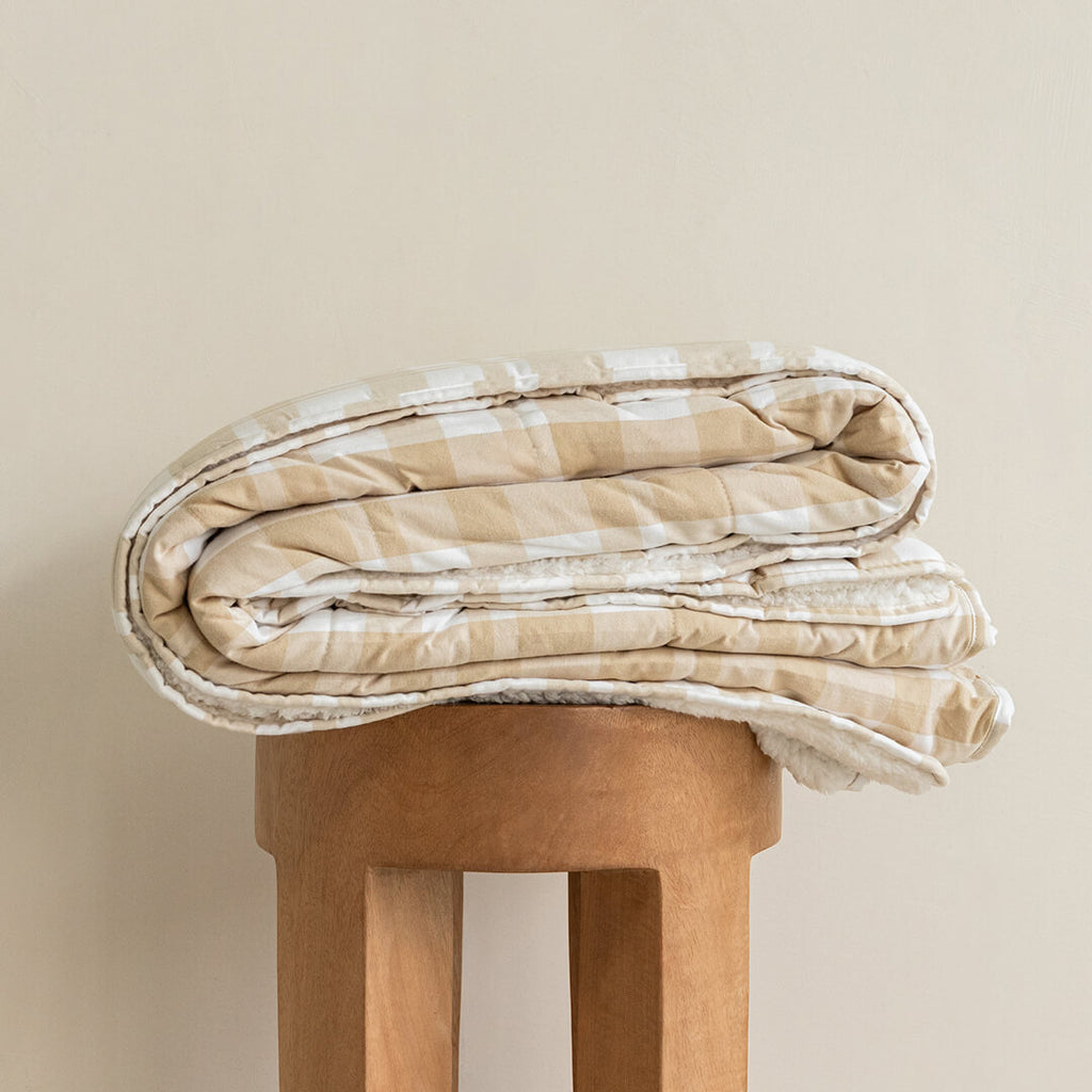Folded beige and white checkered blanket on a wooden stool against a beige background.