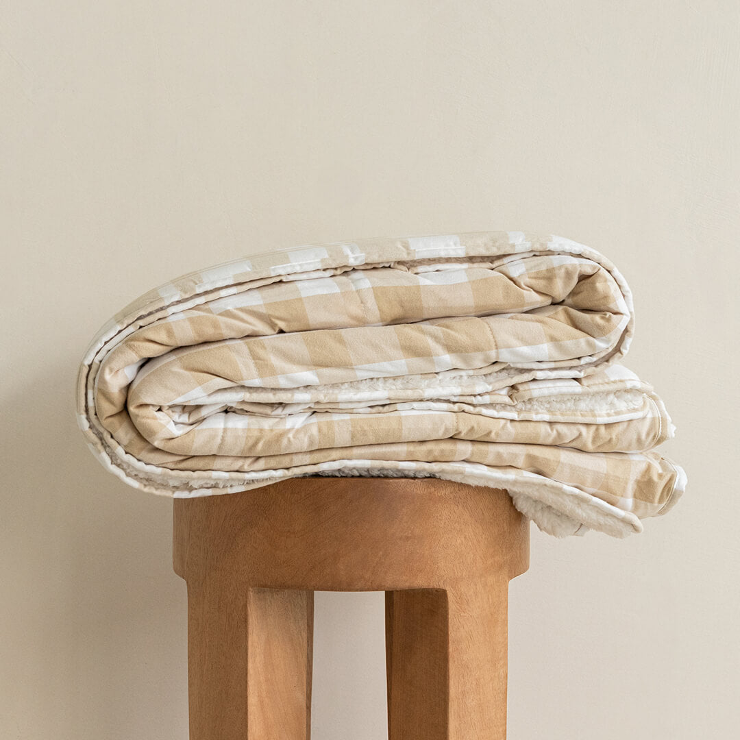 Folded beige and white checkered blanket on a wooden stool against a beige background.