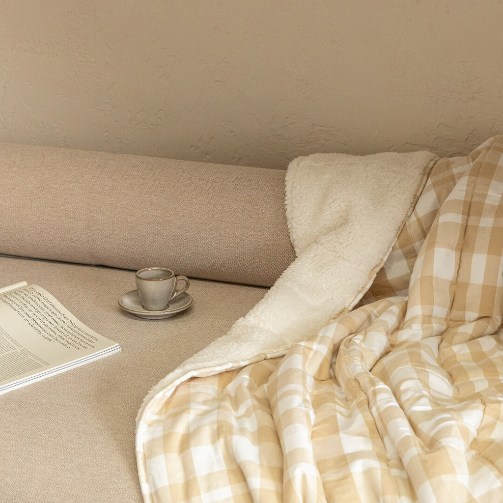 Cozy corner with a blanket, cup of coffee, and laptop on a beige couch.