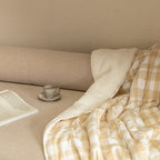 Cozy corner with a blanket, cup of coffee, and laptop on a beige couch.