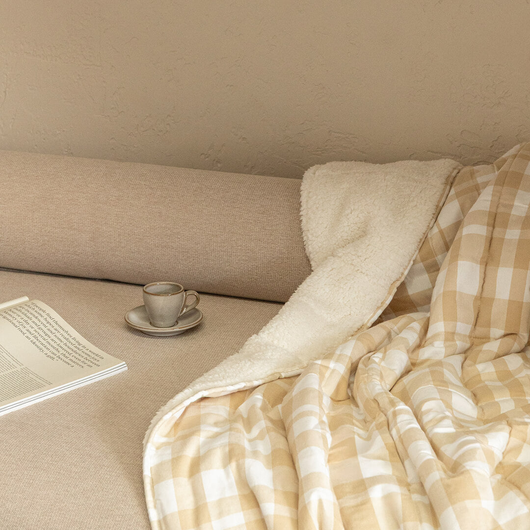Cozy corner with a blanket, cup of coffee, and laptop on a beige couch.