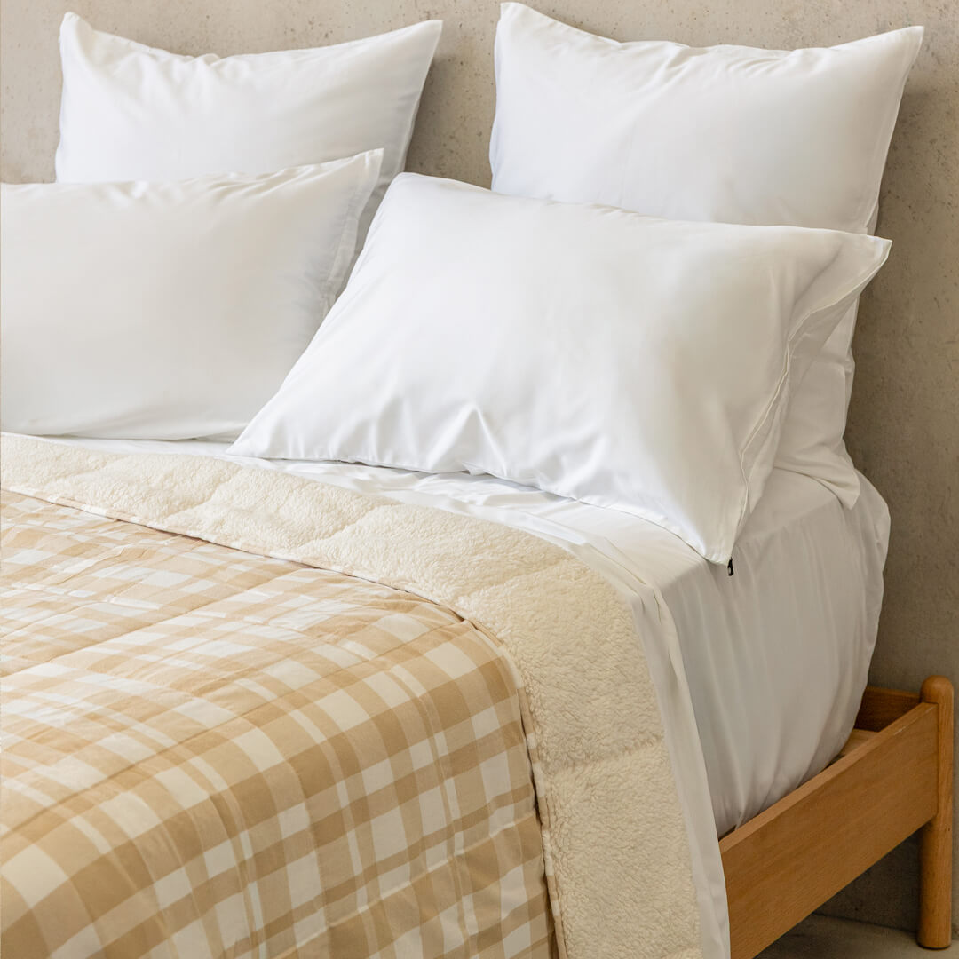 Bed with white pillows and a beige checkered blanket against a neutral wall.
