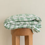 Green and white checkered blanket on a wooden stool against a beige background.