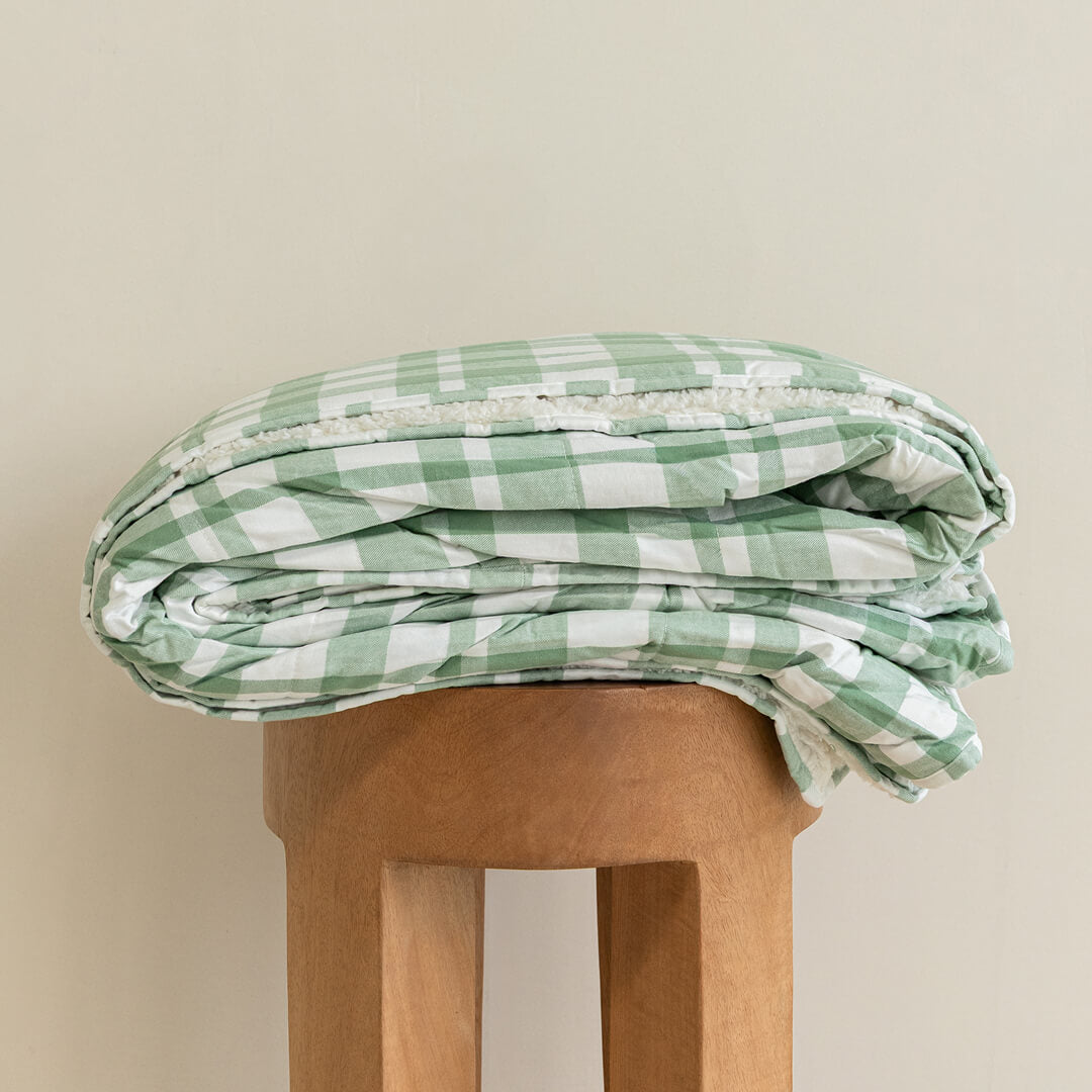 Green and white checkered blanket on a wooden stool against a beige background.