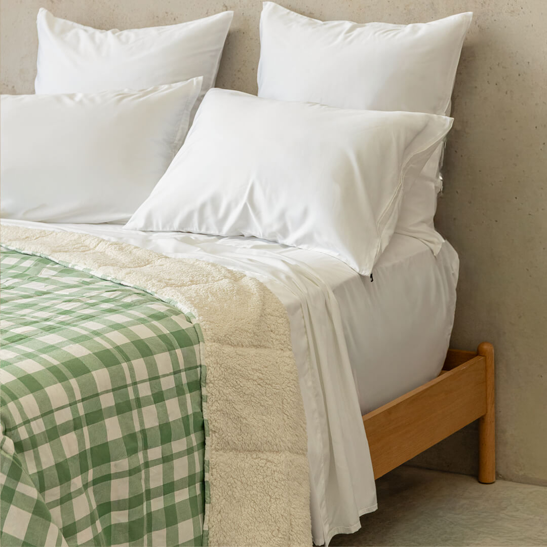 Bed with white bedding, green plaid blanket, and wooden headboard.