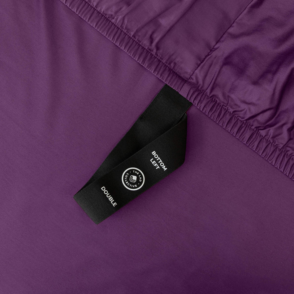 Close up of fitted sheet corner strap in purple bedding