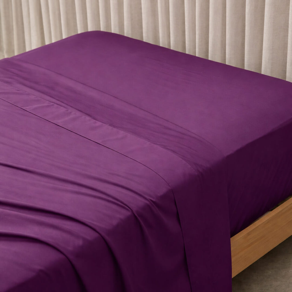 Purple bed sheets on a bed with a neutral background.
