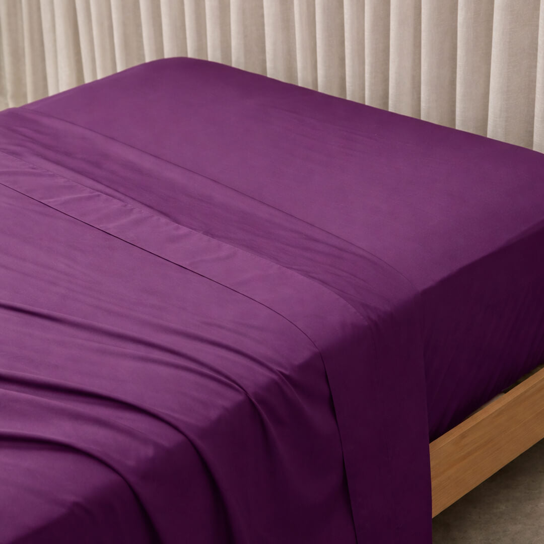 Purple bed sheets on a bed with a neutral background.