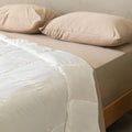 Beige bed with white quilt insert and pillows on a neutral background.