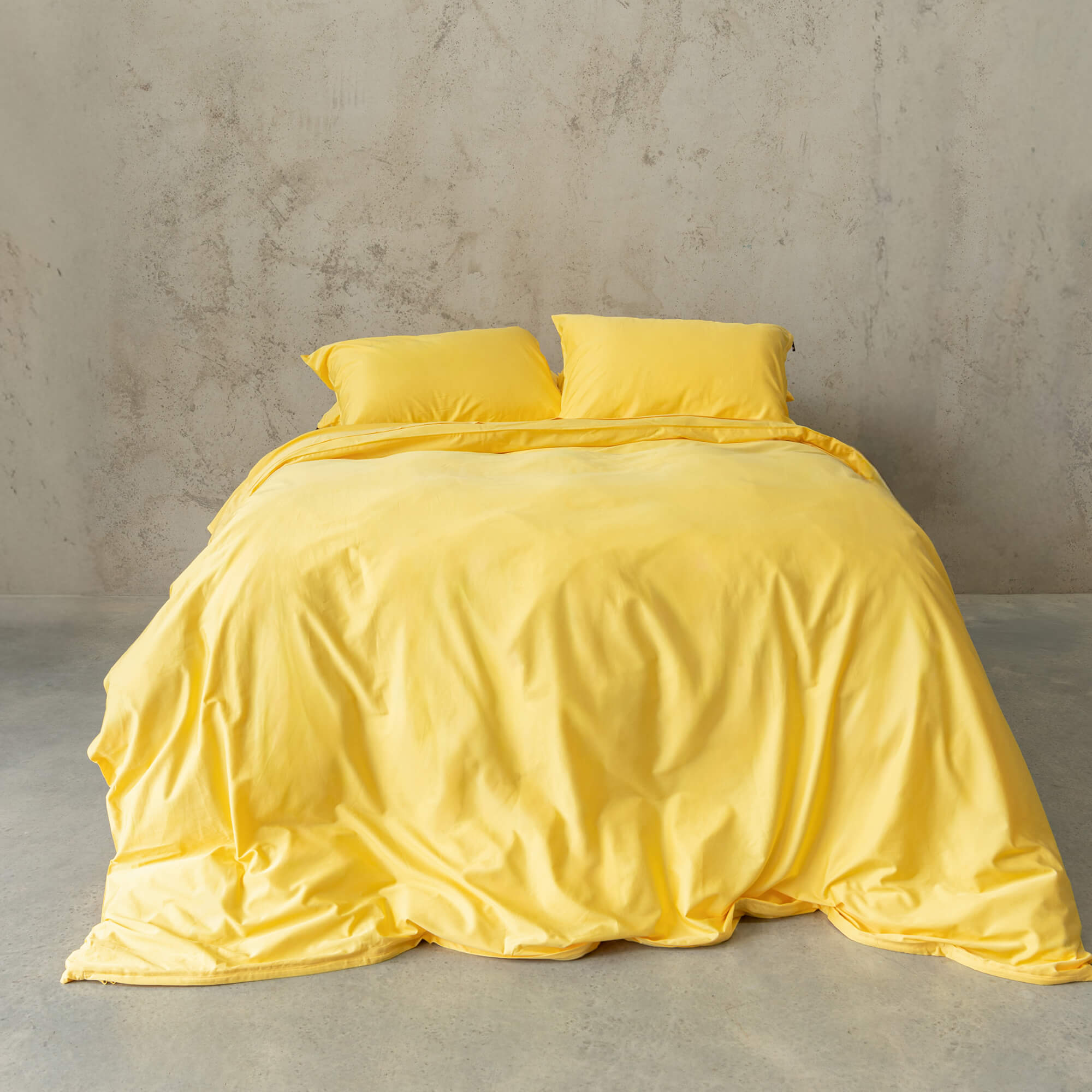 Bright yellow quilt cover set on a bed, against a neutral concrete look backdrop.