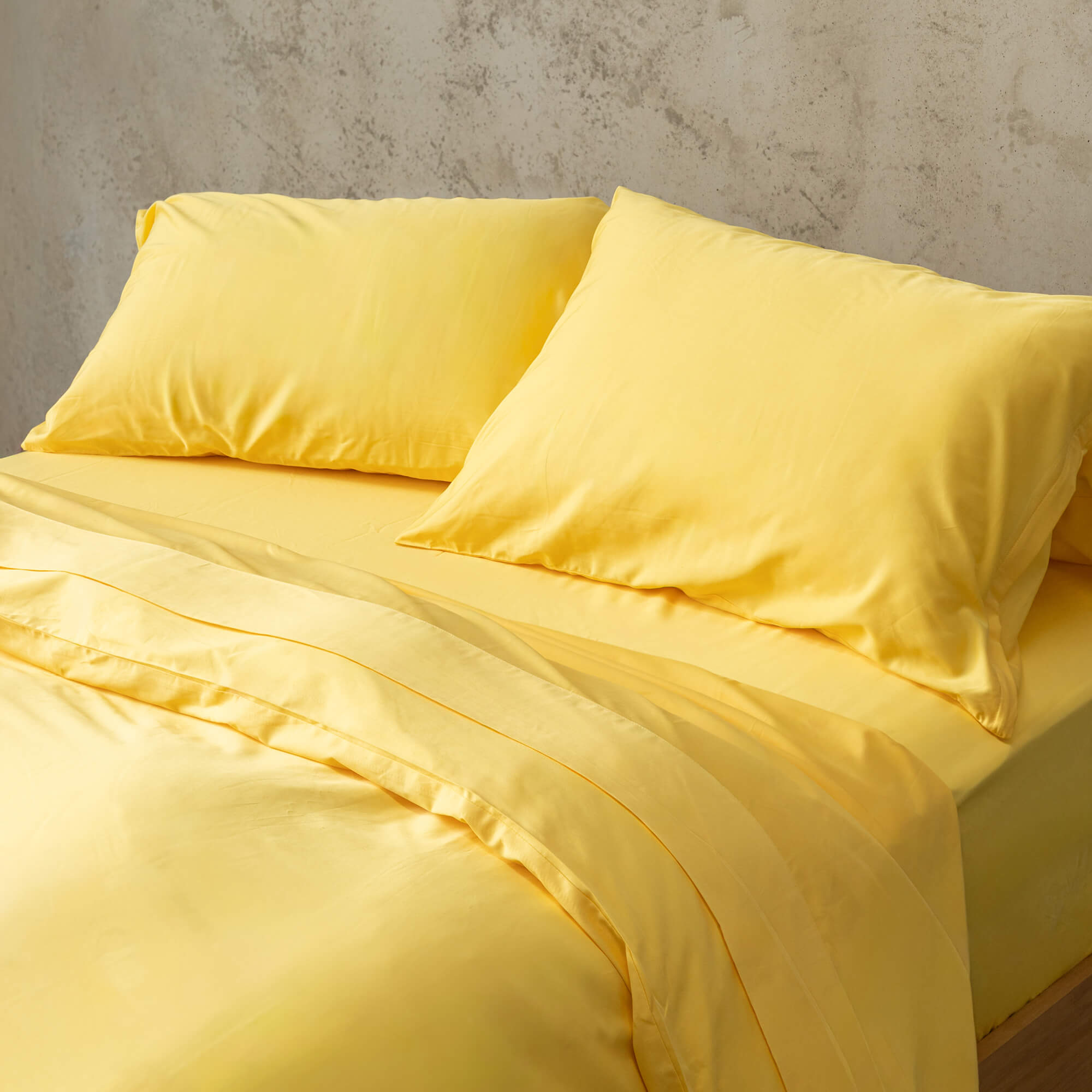 Bright yellow quilt cover set on a bed, against a neutral concrete look backdrop.