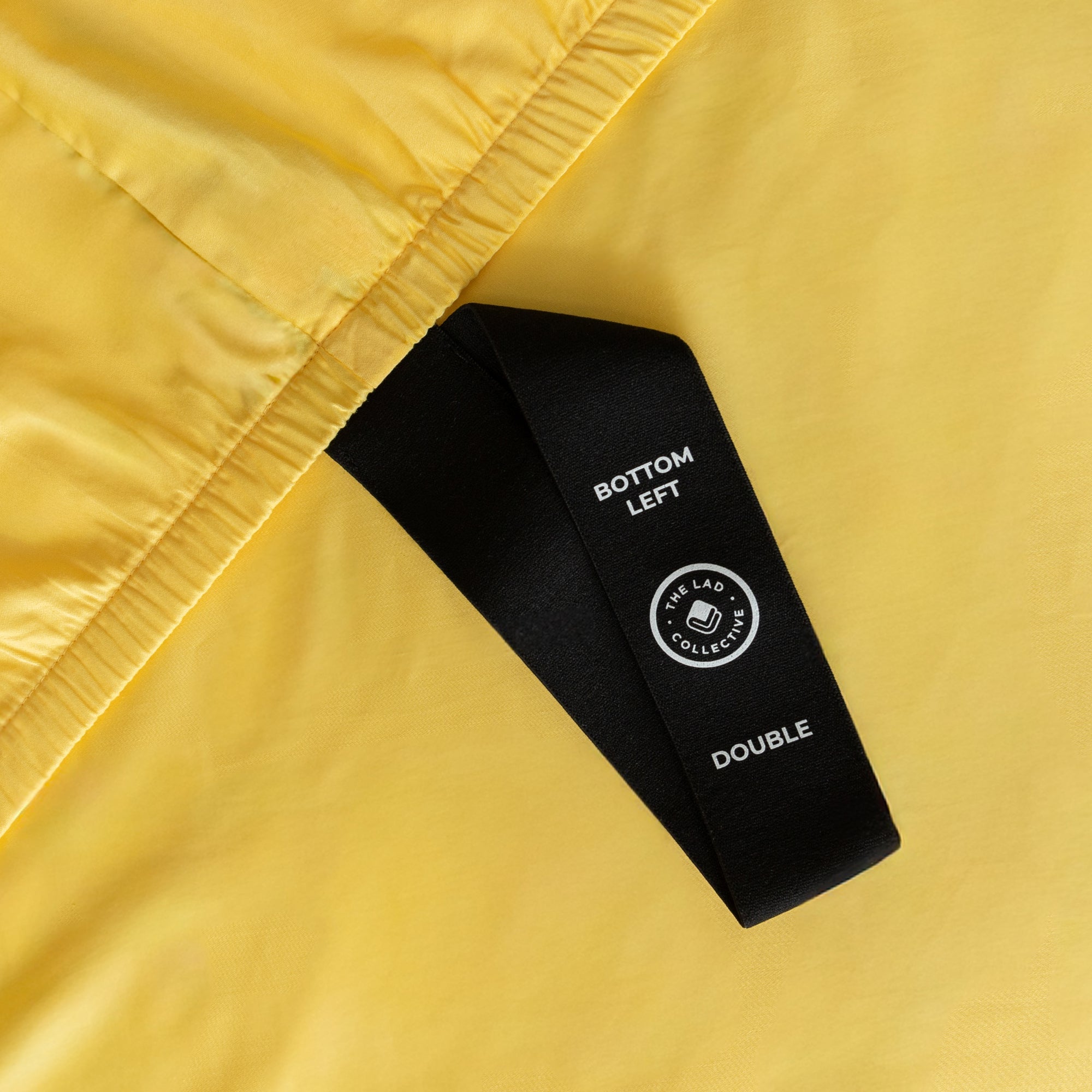 Close up of bright yellow fitted sheet labelled corner loop strap that reads 'Bottom Left' and 'Double.