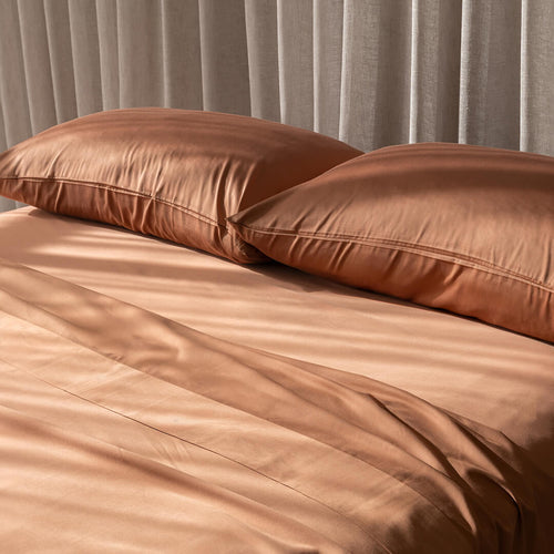 Brown pillows on a matching brown sheets with neutral curtains in the background.