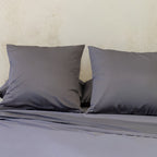 Grey bedding set with two pillows on a bed against a beige wall.