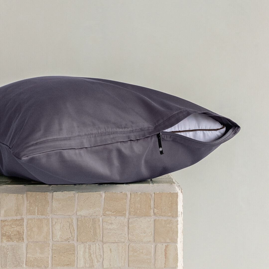 Dark grey pillow on a textured surface with a neutral background.