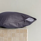 Dark grey pillow on a textured surface with a neutral background.