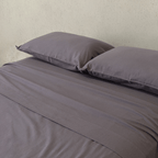 Close-up of a charcoal grey fitted sheet and matching pillowcases, highlighting the smooth texture, soft finish, and coordinated bedding design.