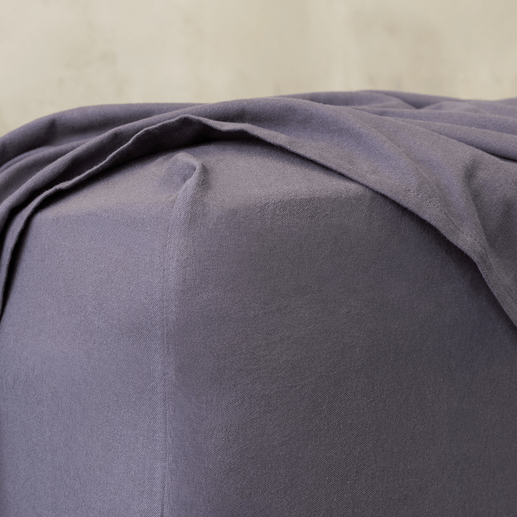 Close-up of a charcoal grey fitted sheet corner, highlighting the elasticized edge designed for a secure and snug mattress fit.
