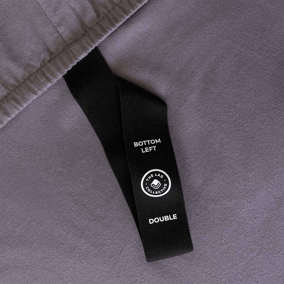 Close-up of a fitted sheet orientation tag labeled “Bottom Left,” designed to simplify bed-making and ensure correct sheet placement.