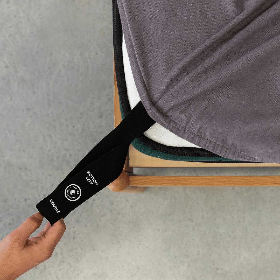 Charcoal grey fitted sheet with an orientation tag extended from the mattress corner, demonstrating the easy-to-identify labeling system for quick bed setup.