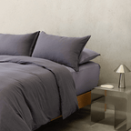 Styled dark stone gray bedding with matching pillows beside a metallic bedside table and silver lamp.