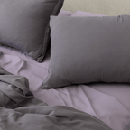 Close-up of dark stone gray pillows arranged over lighter gray bedding with the matching quilt cover softly gathered in front.
