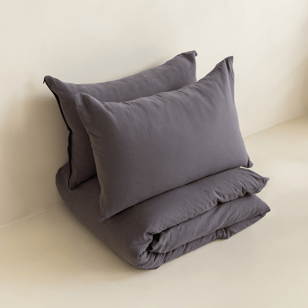 Two dark stone gray pillows arranged above a folded matching quilt cover in a minimal studio setting.