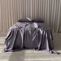 Bed with gray bedding and pillows against a beige curtain background