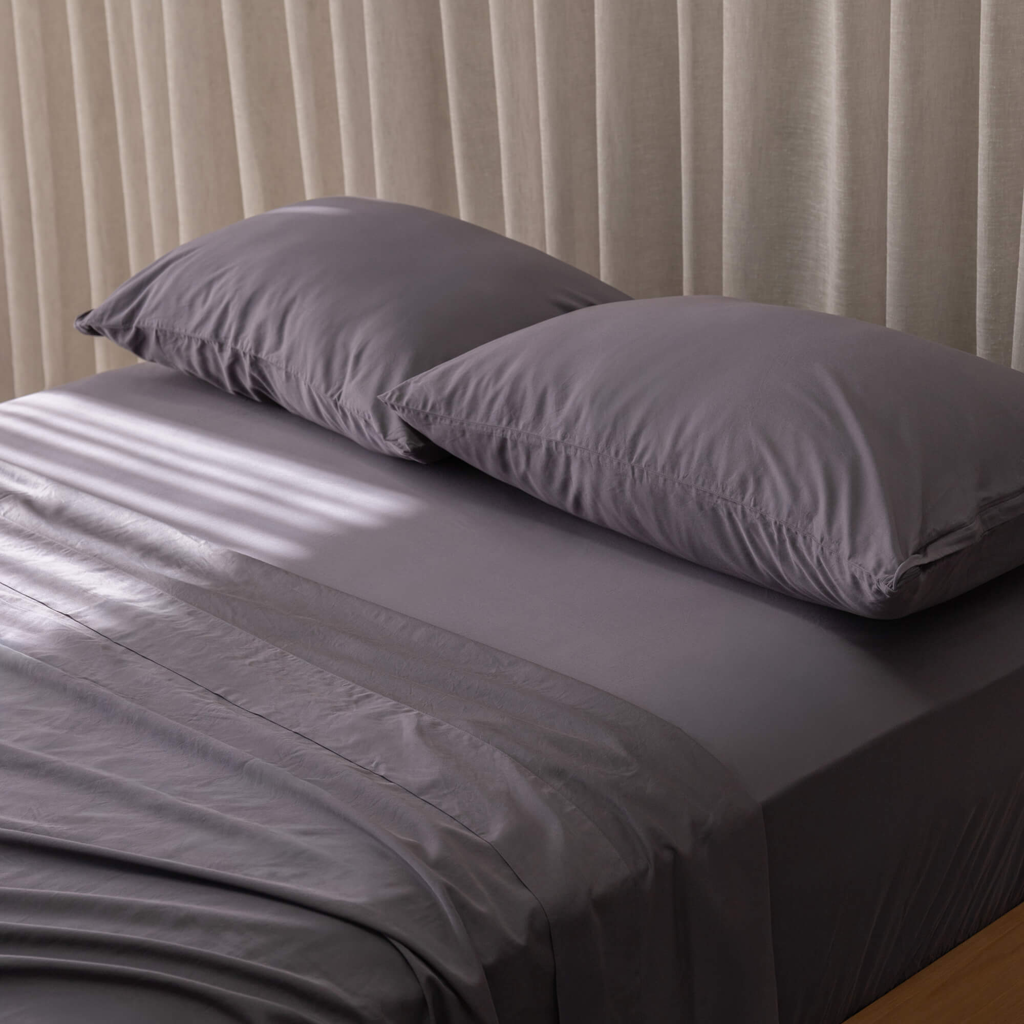 Gray bedspread and pillows on a bed with beige curtains in the background