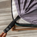 Person adjusting a charcoal gray fitted sheet with a black strap on a gray surface