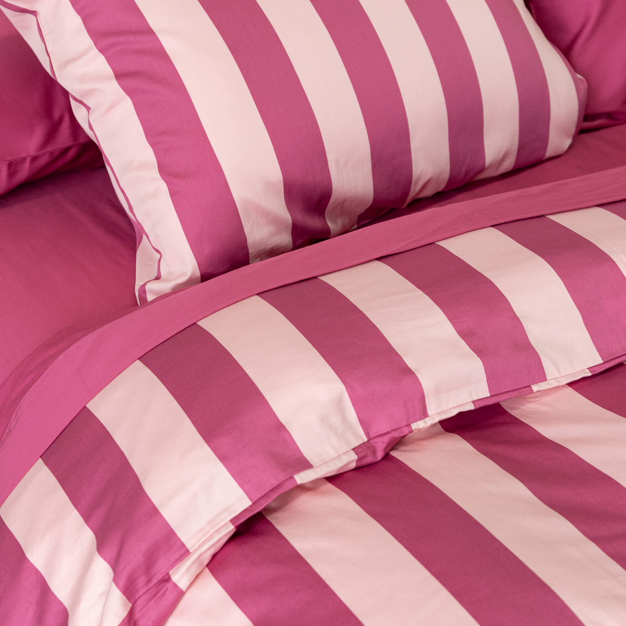 Close-up details of a raspberry pink stripe quilt cover set on a bed.
