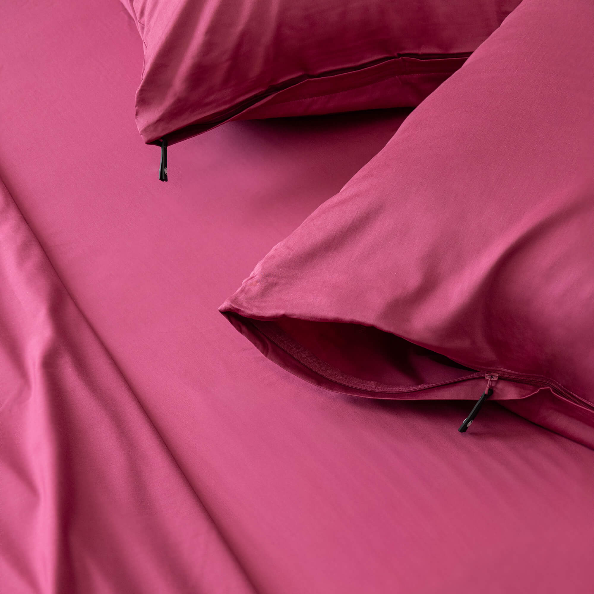 Close up of two invisible zip raspberry pink pillowcases on a bed that has the matching sheets.