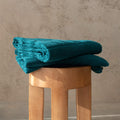 Stack of teal towels on a wooden stool against a beige wall.