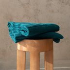 Stack of teal towels on a wooden stool against a beige wall.