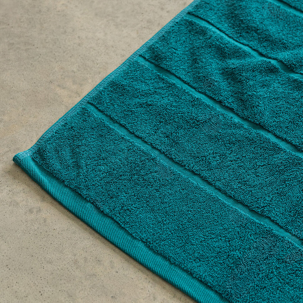 Teal bath towel on a beige floor.