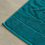 Teal bath towel on a beige floor.