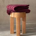 Folded burgundy towel on a wooden stool against a neutral background