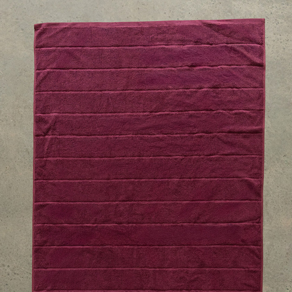 Burgundy bath towel on a beige wall.