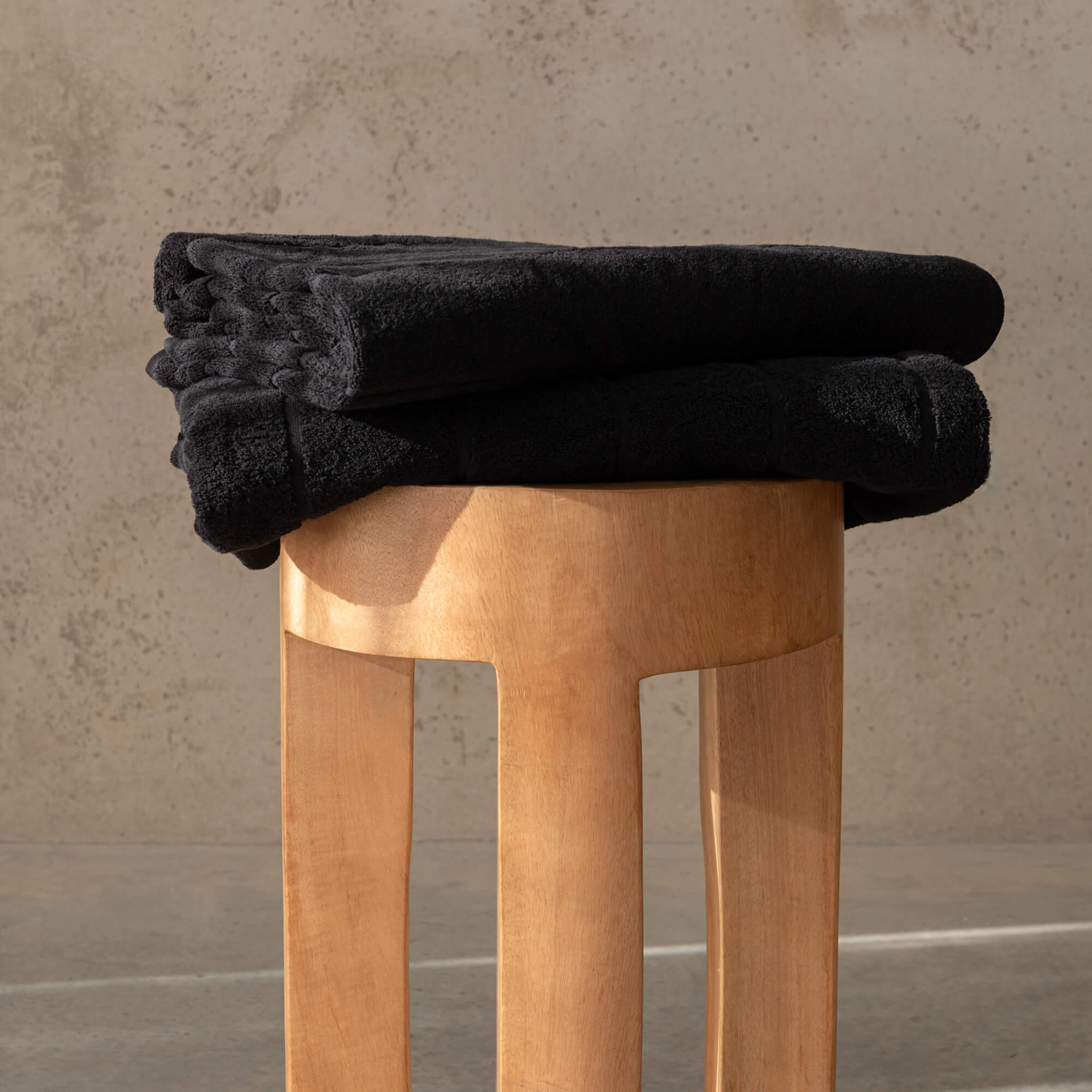 Stack of black towels on a wooden stool against a beige wall.