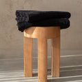 Stack of black towels on a wooden stool against a beige wall.